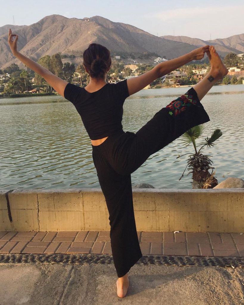Sandra Rovegno haciendo una postura de yoga frente a una laguna.