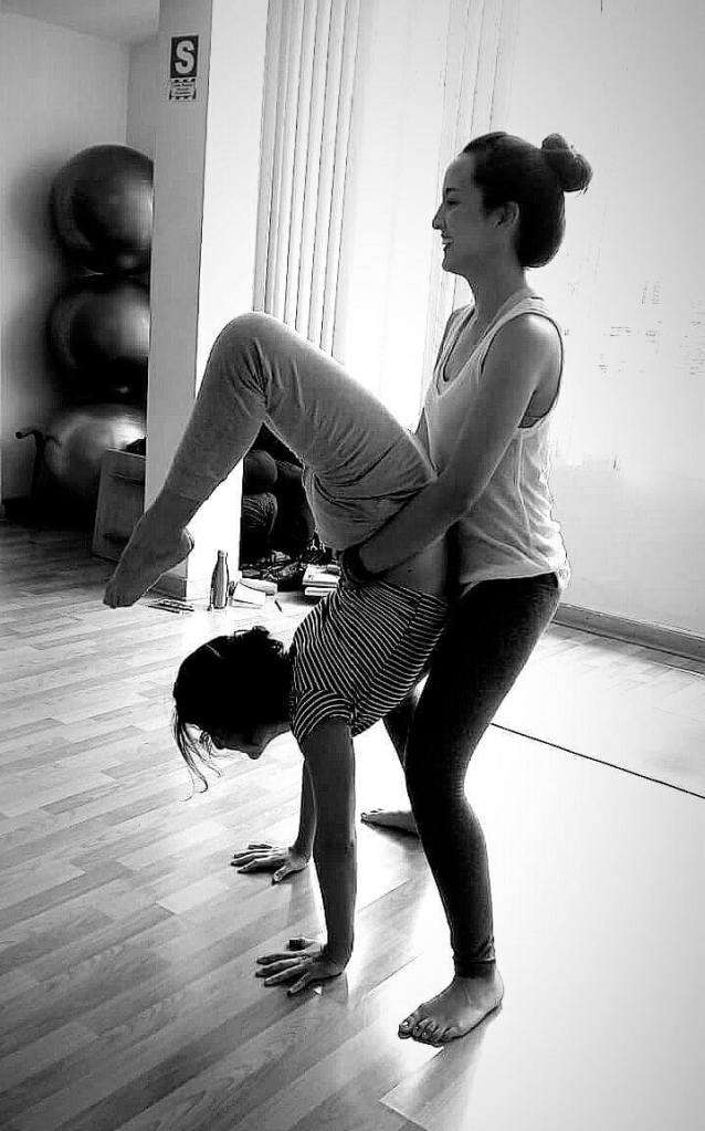 Sandra Rovegno ayudando a una alumna a ponerse en una posición de yoga. Es una imagen promocional para la página Yoga en Oviedo, Asturias.